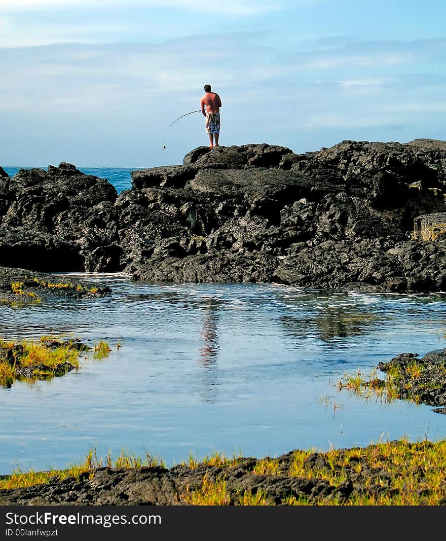 Man using rod and reel to fish from atop lava outcropping. Man using rod and reel to fish from atop lava outcropping