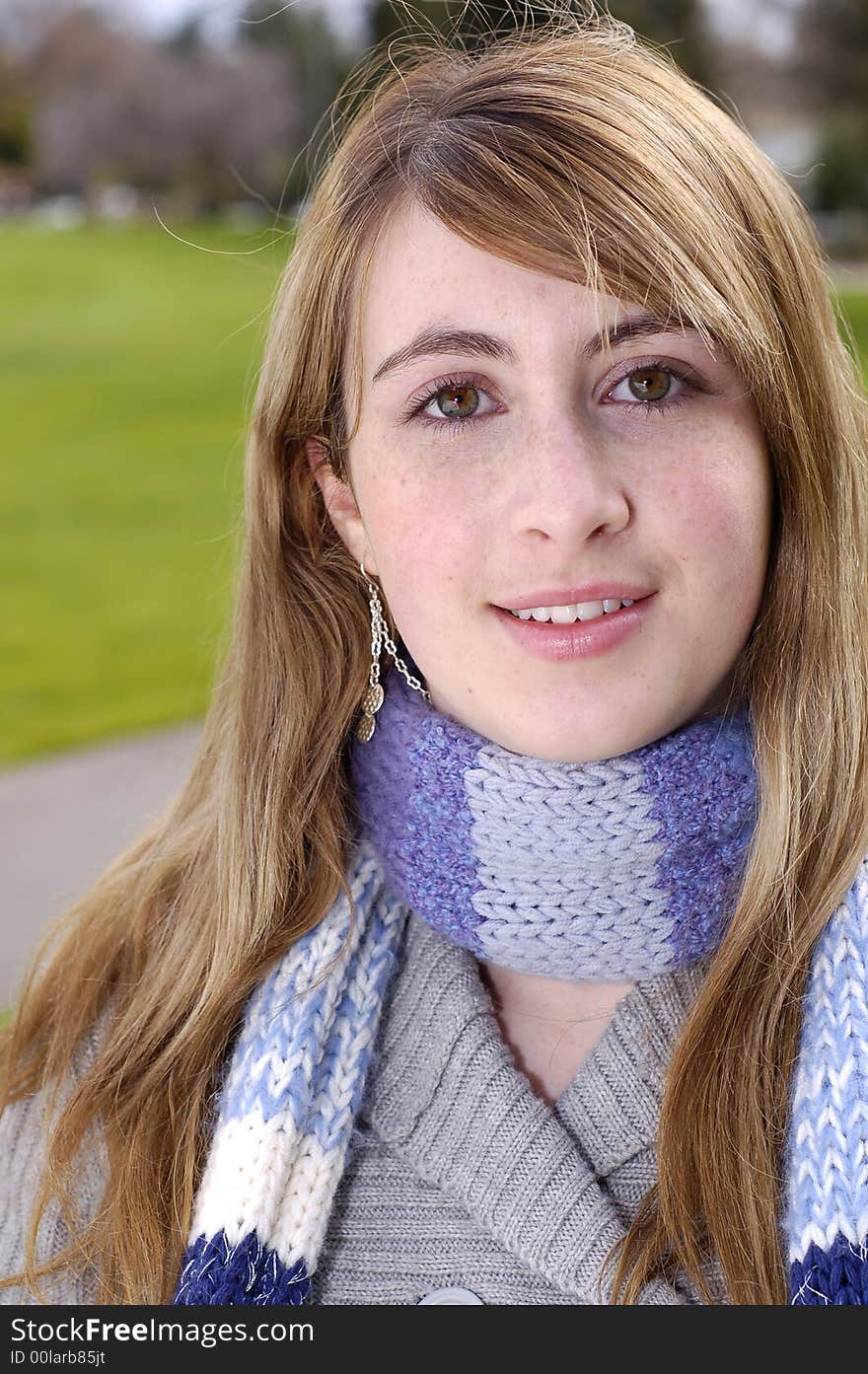 Young beautiful teen outdoors at the park with a different pose, scarf, and sweater. Has a fall or winter season look.