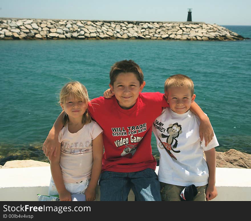 Three siblings all sat on a wall with a the port entrance to Puerto Duquesa behind them. Three siblings all sat on a wall with a the port entrance to Puerto Duquesa behind them