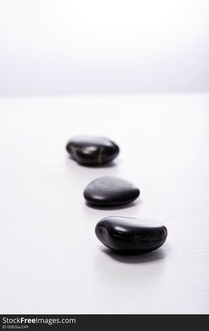 Three smooth, black Zen-Stones (Pebbles) in a row. Focus on front stone. Three smooth, black Zen-Stones (Pebbles) in a row. Focus on front stone.