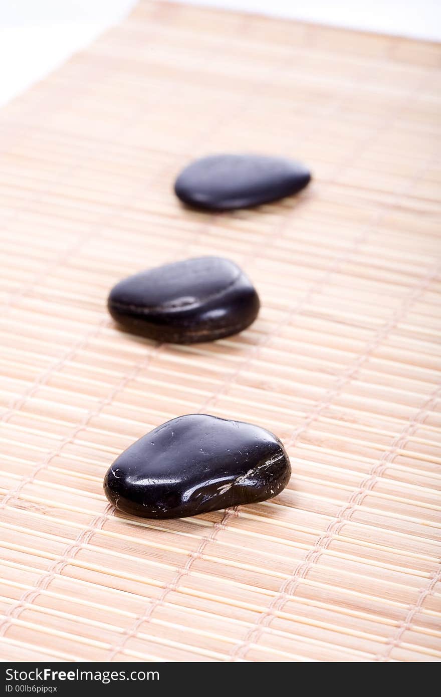 Three smooth, black Zen-Stones (Pebbles) in a row on a bamboomat. Focus on front stone. Three smooth, black Zen-Stones (Pebbles) in a row on a bamboomat. Focus on front stone.