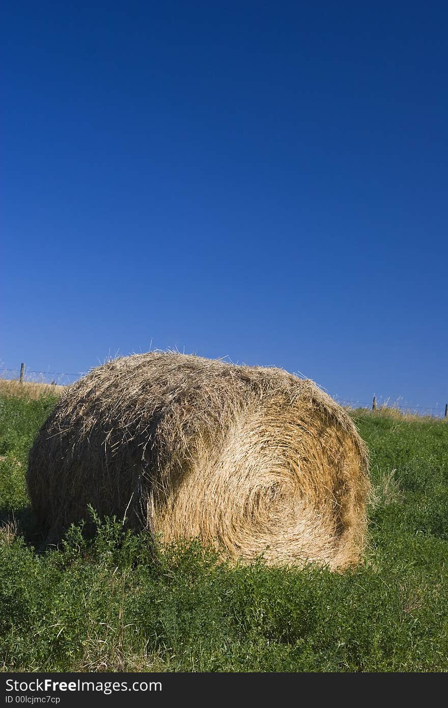 A roll of hay stands on green grass against a deep blue sky.