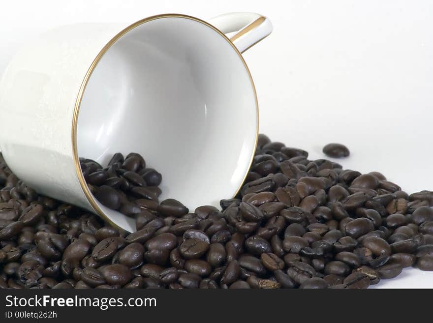 Coffee cup on it's side laying in a pile of coffee beans. Coffee cup on it's side laying in a pile of coffee beans