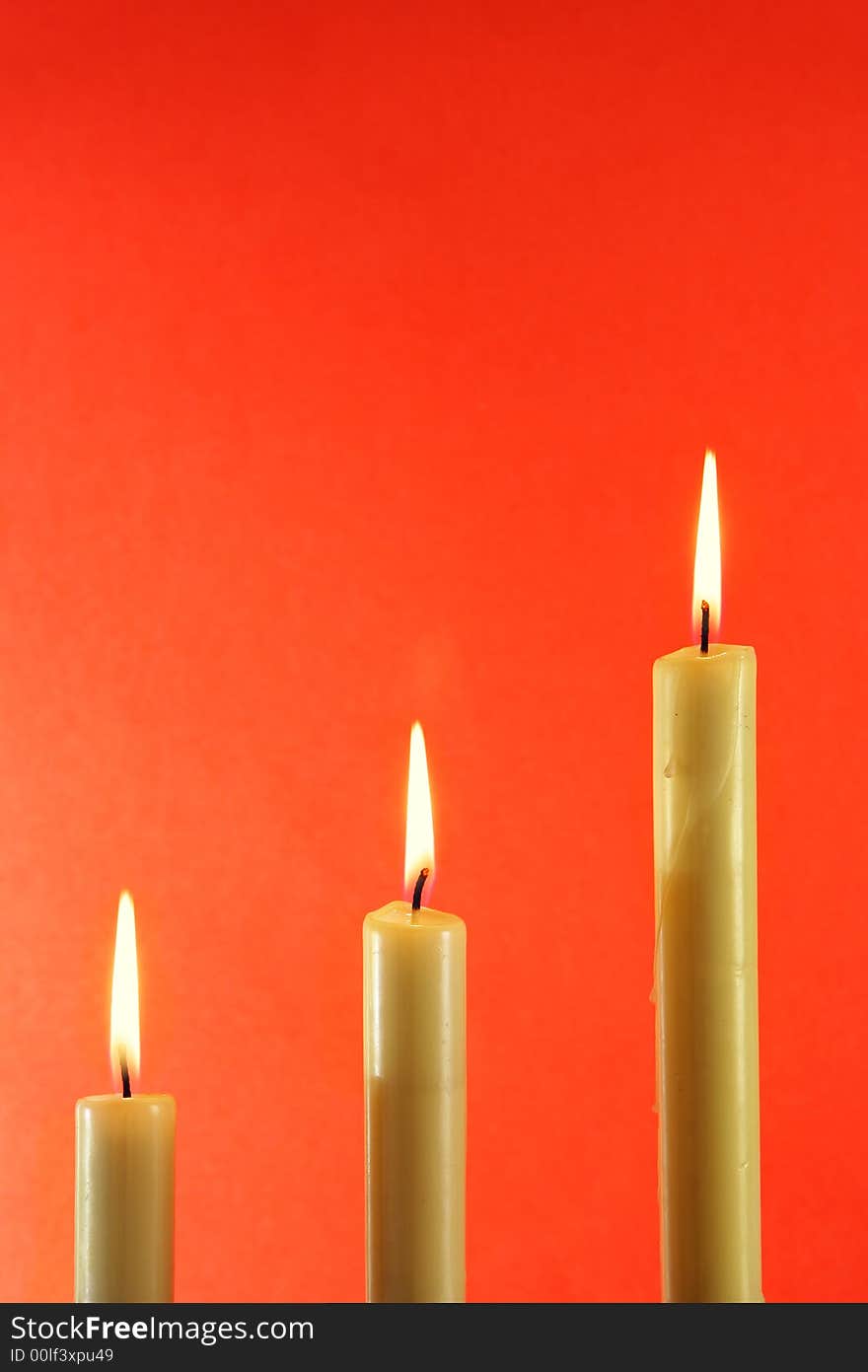 Three burning candles over light red background