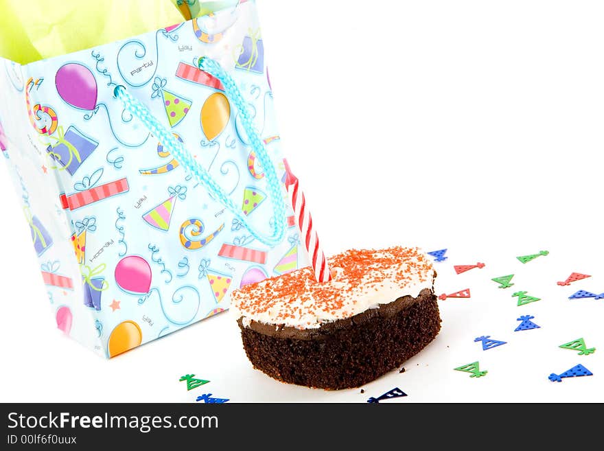 Party hat confetti surrounding a small birthday cake with a single candle and a wrapped gift. Party hat confetti surrounding a small birthday cake with a single candle and a wrapped gift.