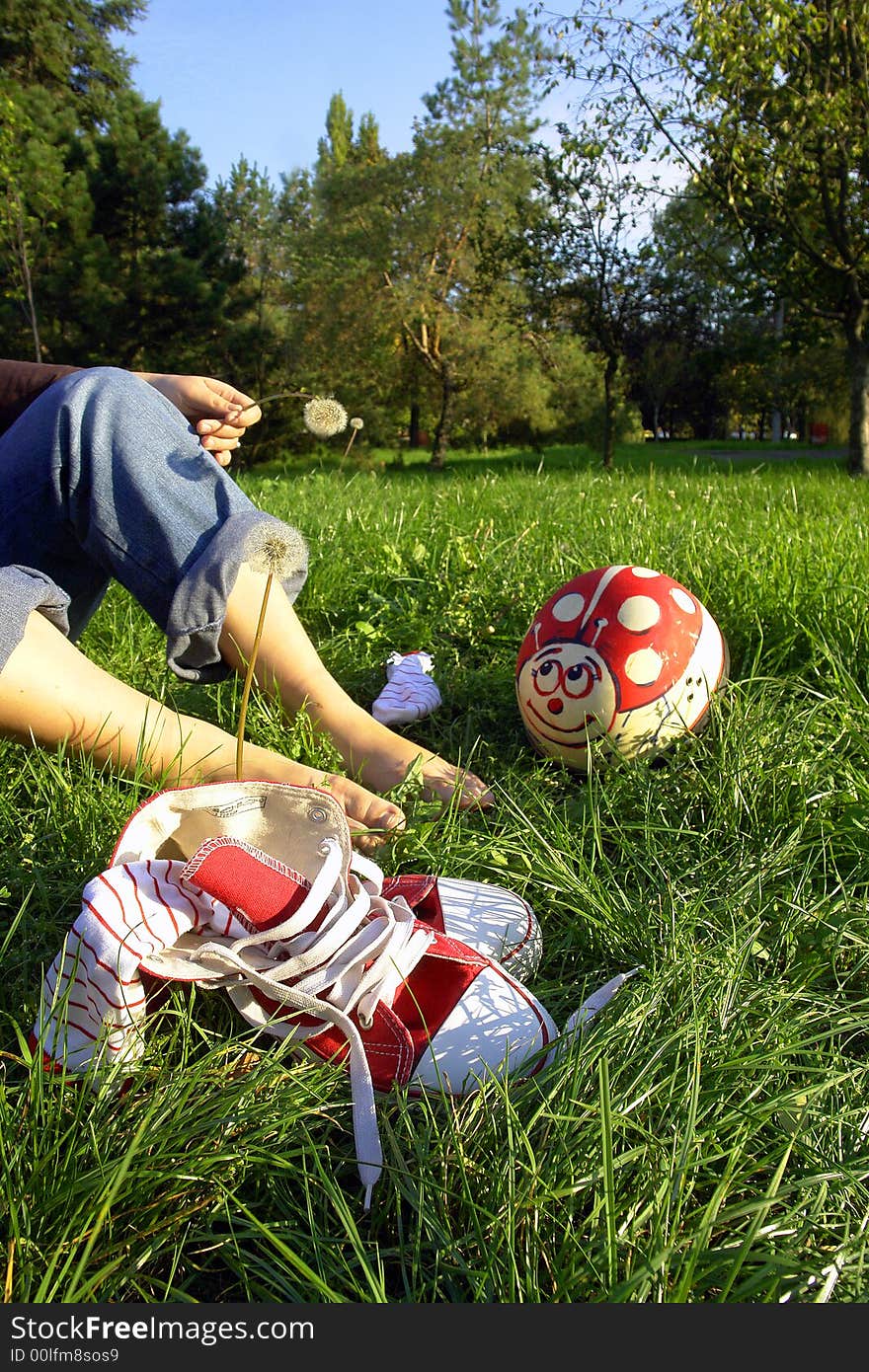 View of girl's legs and her bare feet on grass next to pair of athletic shoes. Face of girl not in photo. View of girl's legs and her bare feet on grass next to pair of athletic shoes. Face of girl not in photo.