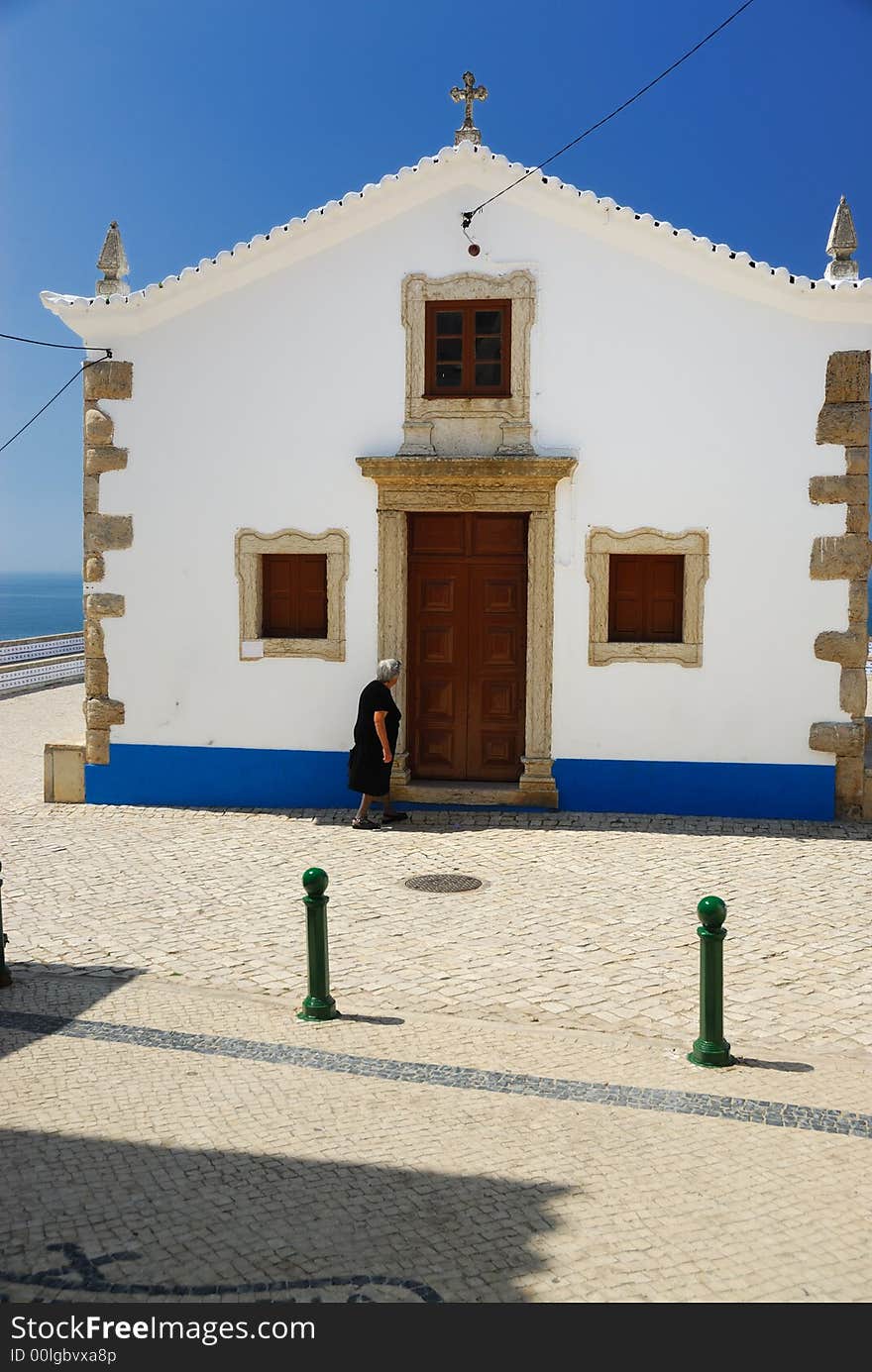 Old woman in black dress is going to the white, small church by the ocean. Old woman in black dress is going to the white, small church by the ocean.