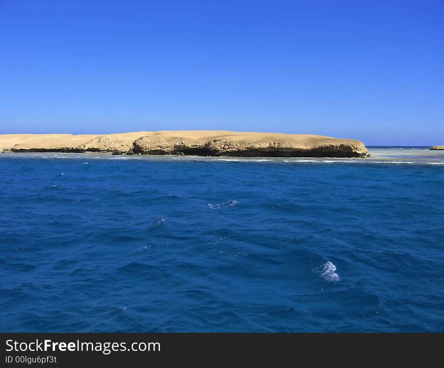 The sandy island located at ocean, among small waves