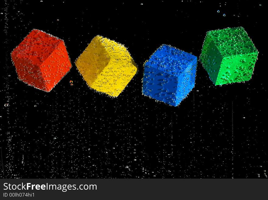 Four brightly colored cubes floating in a clear bubbly liquid on a black background. Four brightly colored cubes floating in a clear bubbly liquid on a black background.