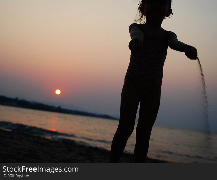 Young kid girl pouring sand on sunset beach