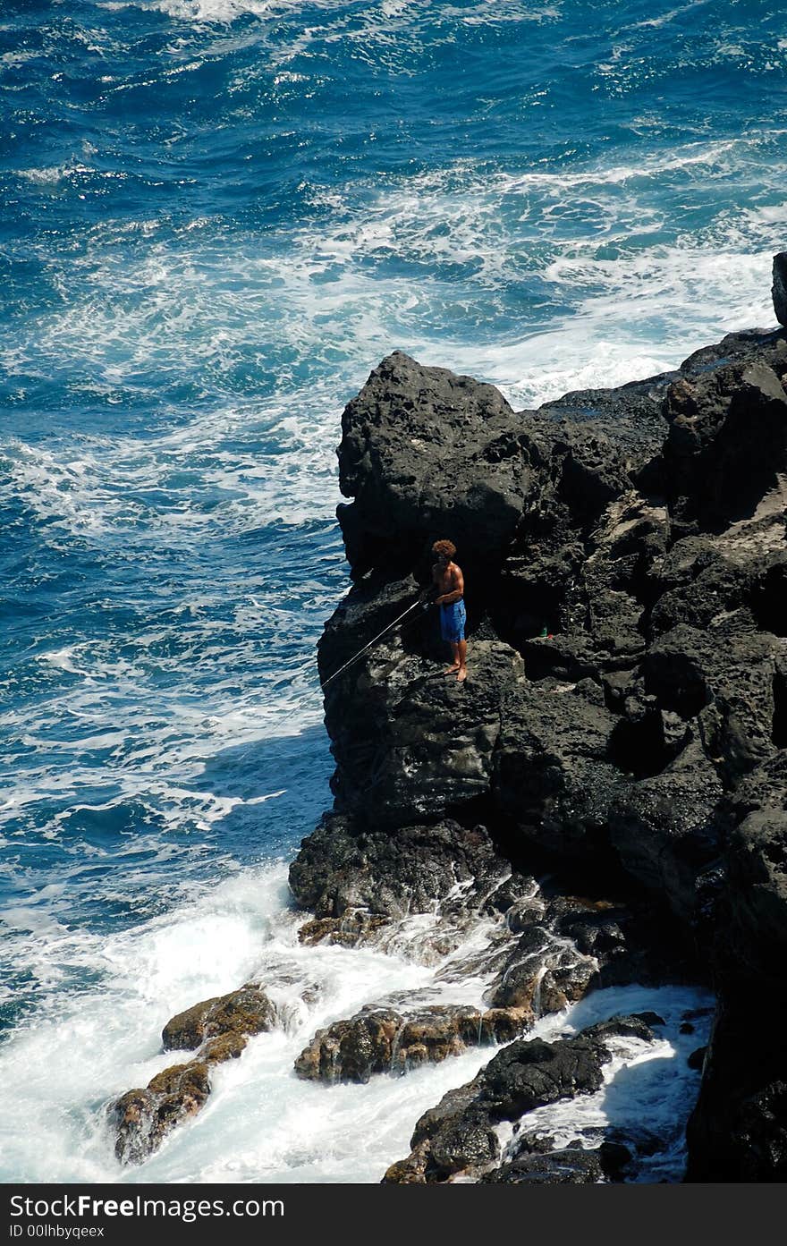 A guy standing and fishing on a black rock. A guy standing and fishing on a black rock