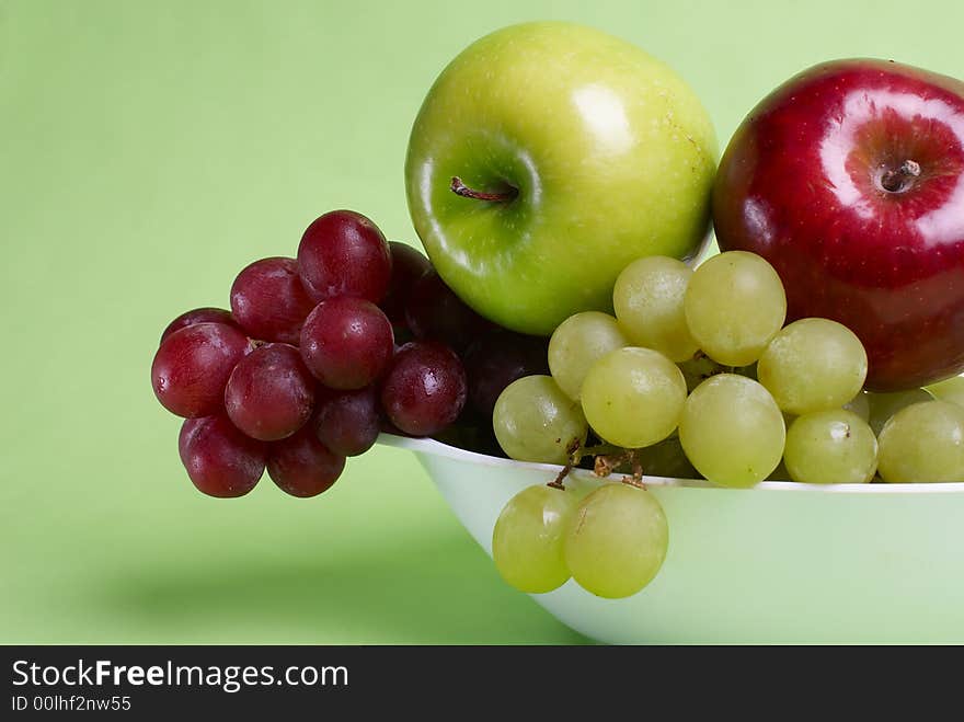 Green and red apples and grapes on plate on green background. Green and red apples and grapes on plate on green background