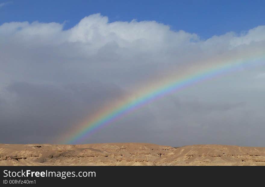 A strong rainbow was created after some rain fall in the desert. Clouds and rainbow. Some blue sky. A strong rainbow was created after some rain fall in the desert. Clouds and rainbow. Some blue sky