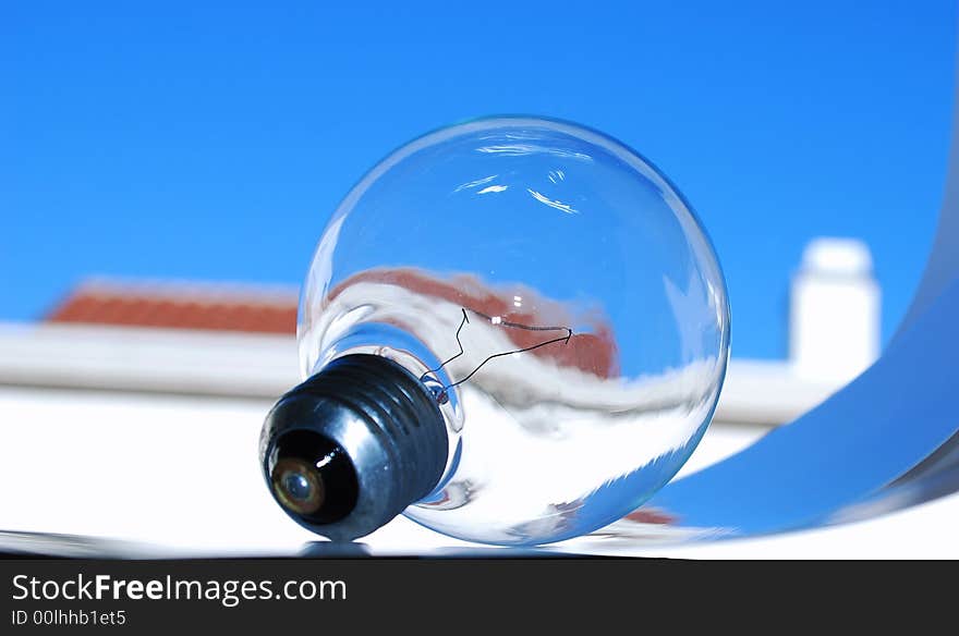 Light Bulb over blue sky, white wall, red roof and chimney in background. Light Bulb over blue sky, white wall, red roof and chimney in background