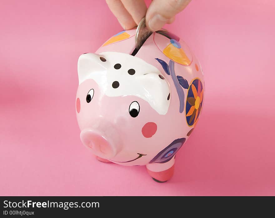 Piggy bank on pink background with hand inserting a silver coin