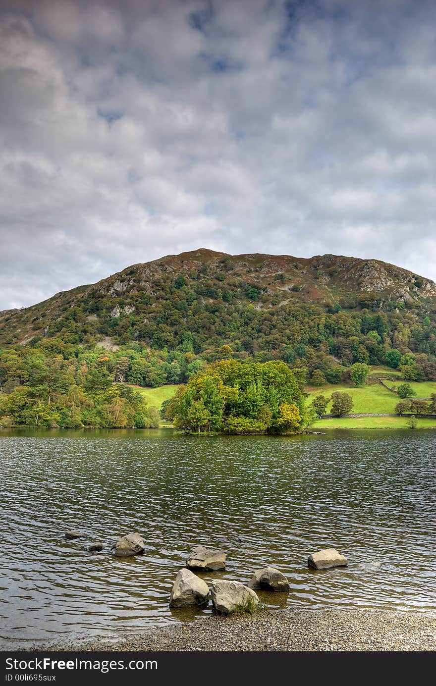 A view of Rydal Water in the English Lake District. There are rocks on the shore and Stratocumulus cloud fills the sky