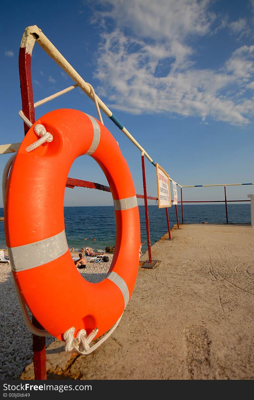 Orange lifebuoy ring on  sea beach on background of  blue sky