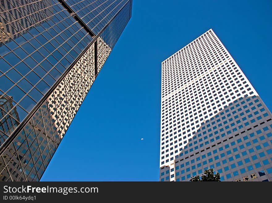 Two tall buildings shot from street level with the moon in between them. Two tall buildings shot from street level with the moon in between them