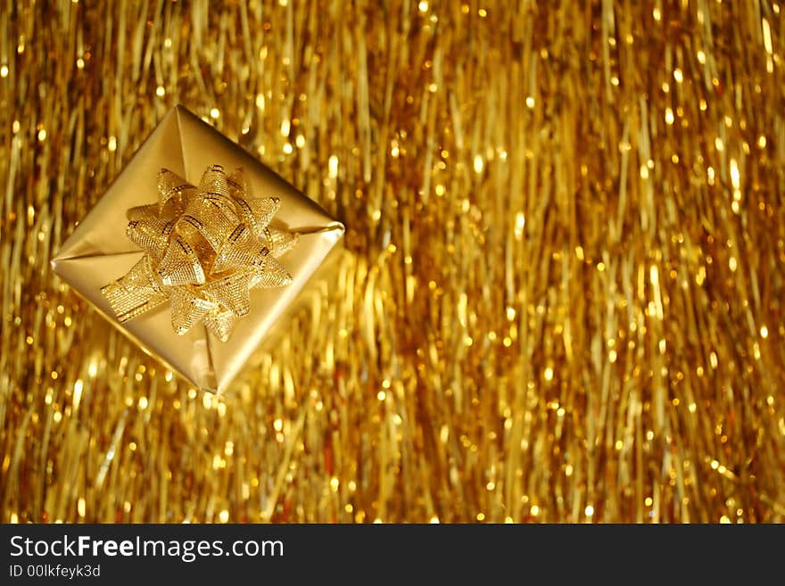 A Christmas box - a golden cube with golden ribbon placed diagonally over golden strings background. A Christmas box - a golden cube with golden ribbon placed diagonally over golden strings background.