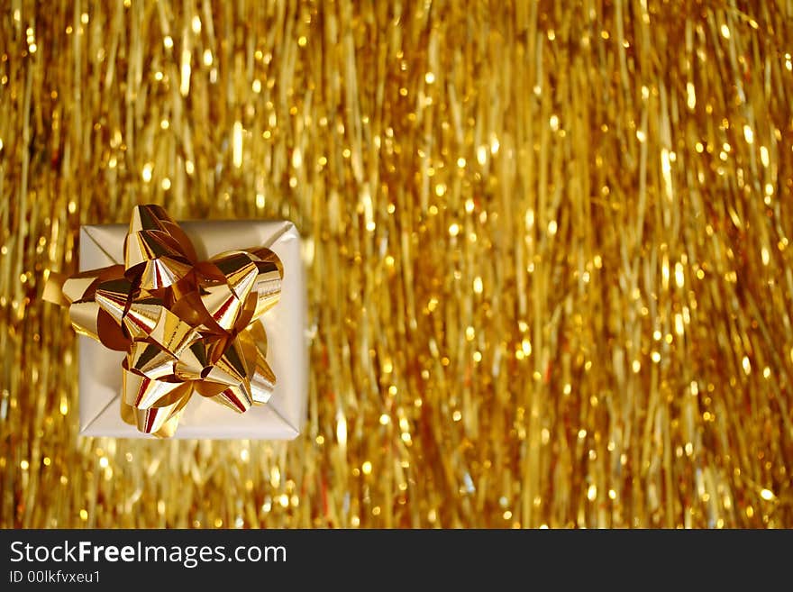 A Christmas box - a slver cube with golden ribbon placed on golden glittering lametta strings. A Christmas box - a slver cube with golden ribbon placed on golden glittering lametta strings.