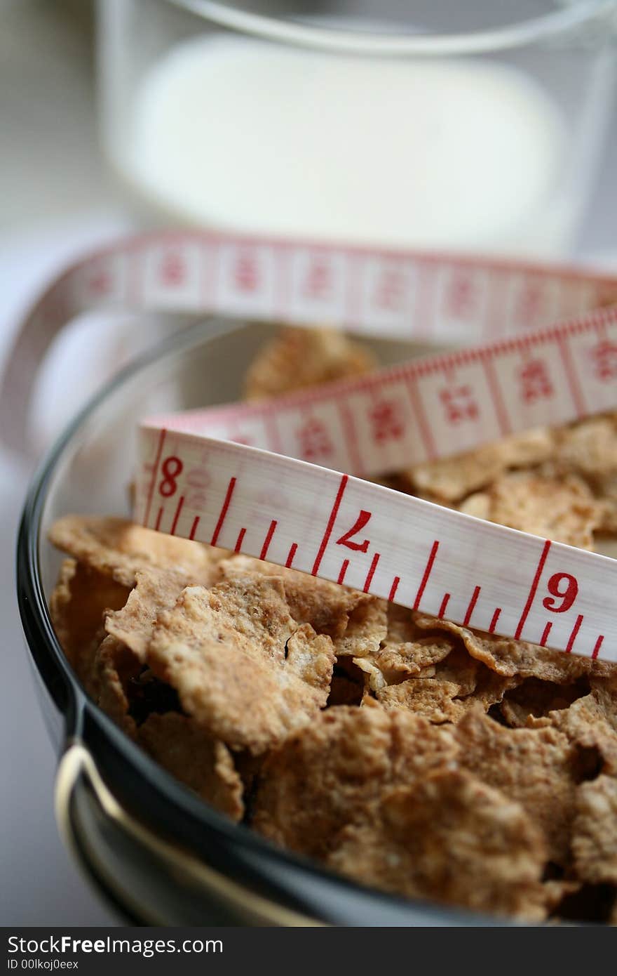 Close-up of a glass of milk, plate with cereal flakes and a measuring tape around it. Close-up of a glass of milk, plate with cereal flakes and a measuring tape around it.