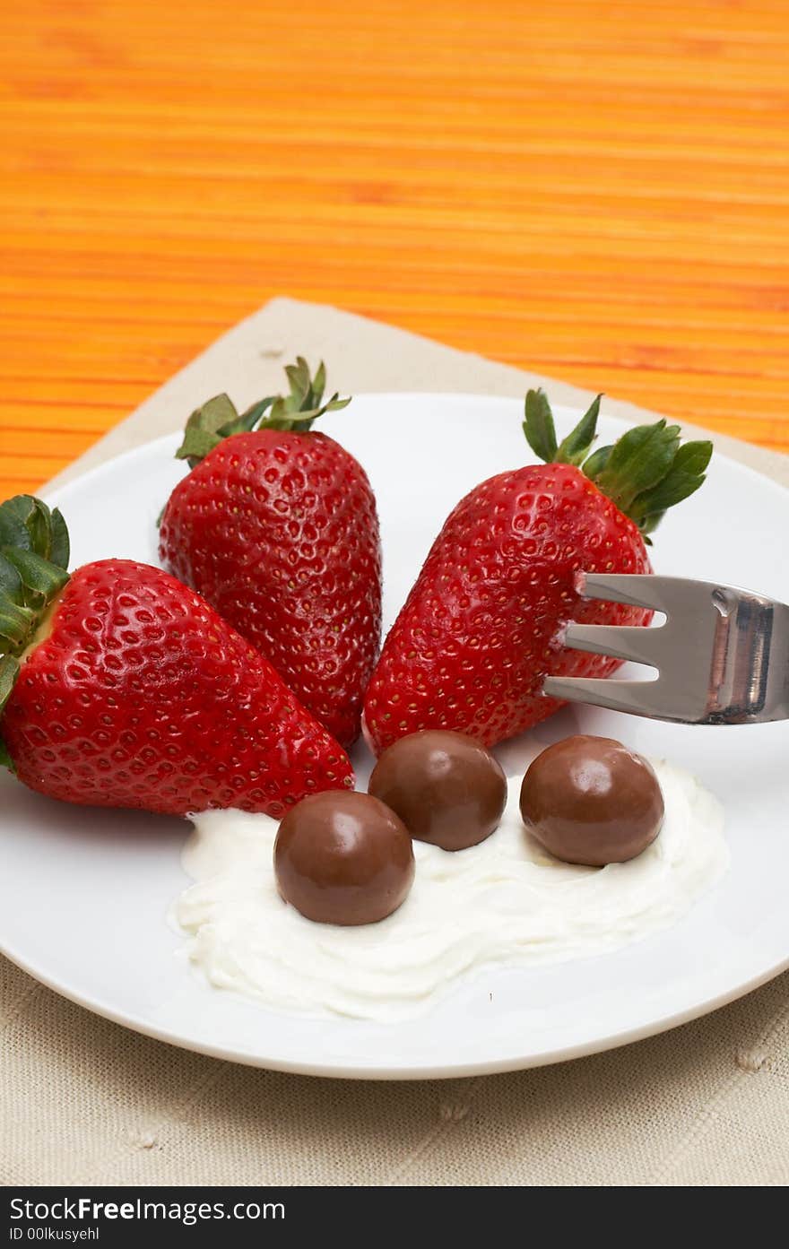 Three strawberries with chocolate balls lying in cream on white saucer. Three strawberries with chocolate balls lying in cream on white saucer