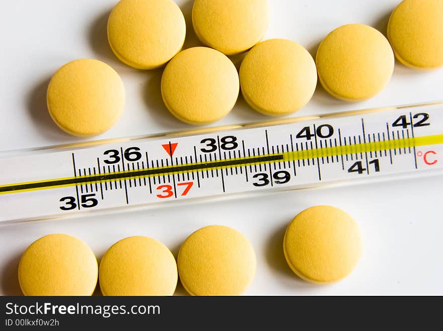 Medical thermometer indicated high temperature and yellow pills over white background. Medical thermometer indicated high temperature and yellow pills over white background