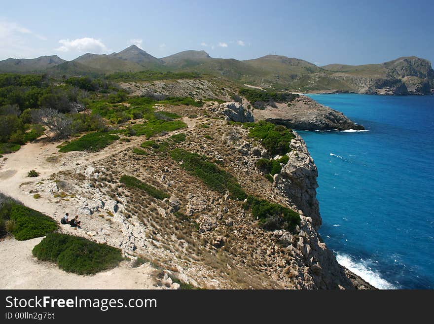 Two wanderers sitting at the coast of Majorca watching the beautiful blue mediterranean sea resting before going on on their path. Two wanderers sitting at the coast of Majorca watching the beautiful blue mediterranean sea resting before going on on their path