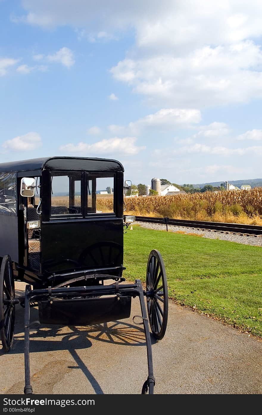 A close up view of the front of an authentic Amish horse-drawn buggy or wagon beside a railroad track with an Amish farm and cornfield in the background. Lancaster County, Pennsylvania (USA)