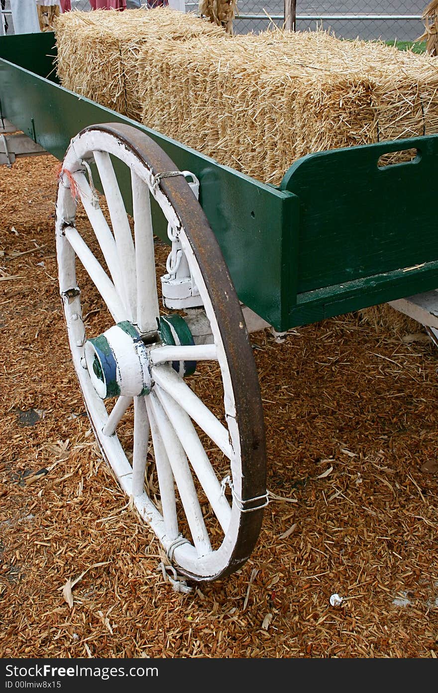 A green wagon with white wheels holds bales of hay.  Hay covers the ground. A green wagon with white wheels holds bales of hay.  Hay covers the ground.