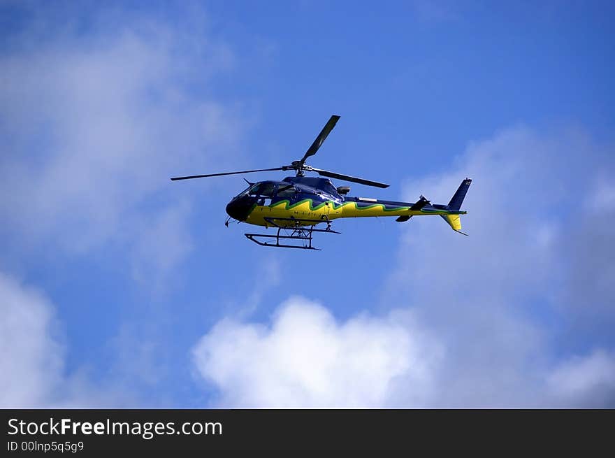 Yellow-blue Helicopter in the sky flying high. Side view. Yellow-blue Helicopter in the sky flying high. Side view.