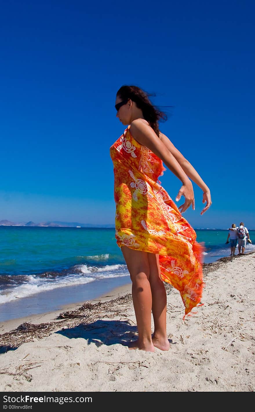 View from side of woman standing on the beach wearning only in orange pareo. View from side of woman standing on the beach wearning only in orange pareo