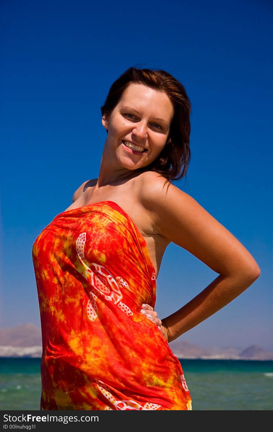 View from side of woman standing on the beach wearning orange pareo placed on the sky. View from side of woman standing on the beach wearning orange pareo placed on the sky