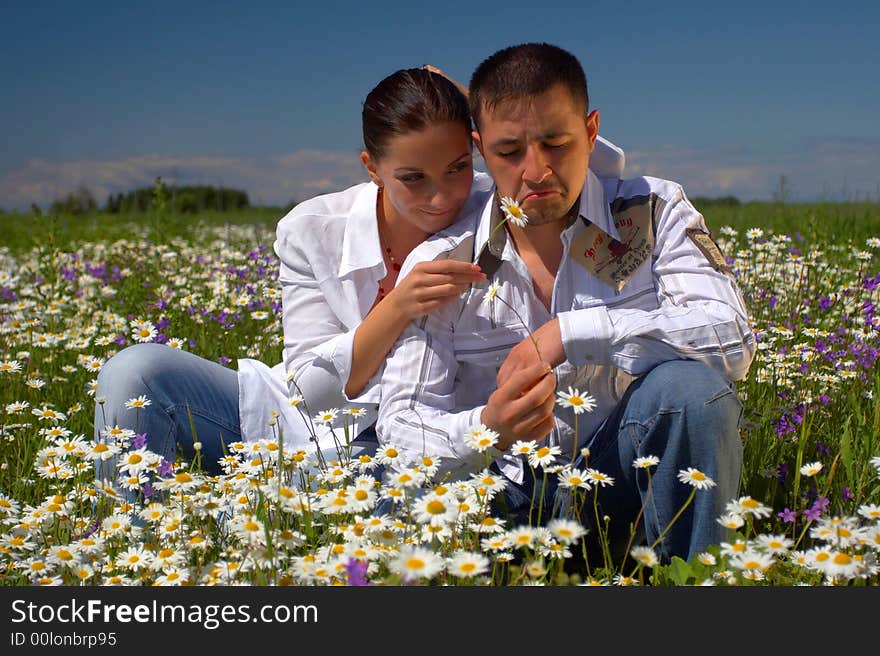 Young happy couple at the sunny day in a field with camomiles and handbells