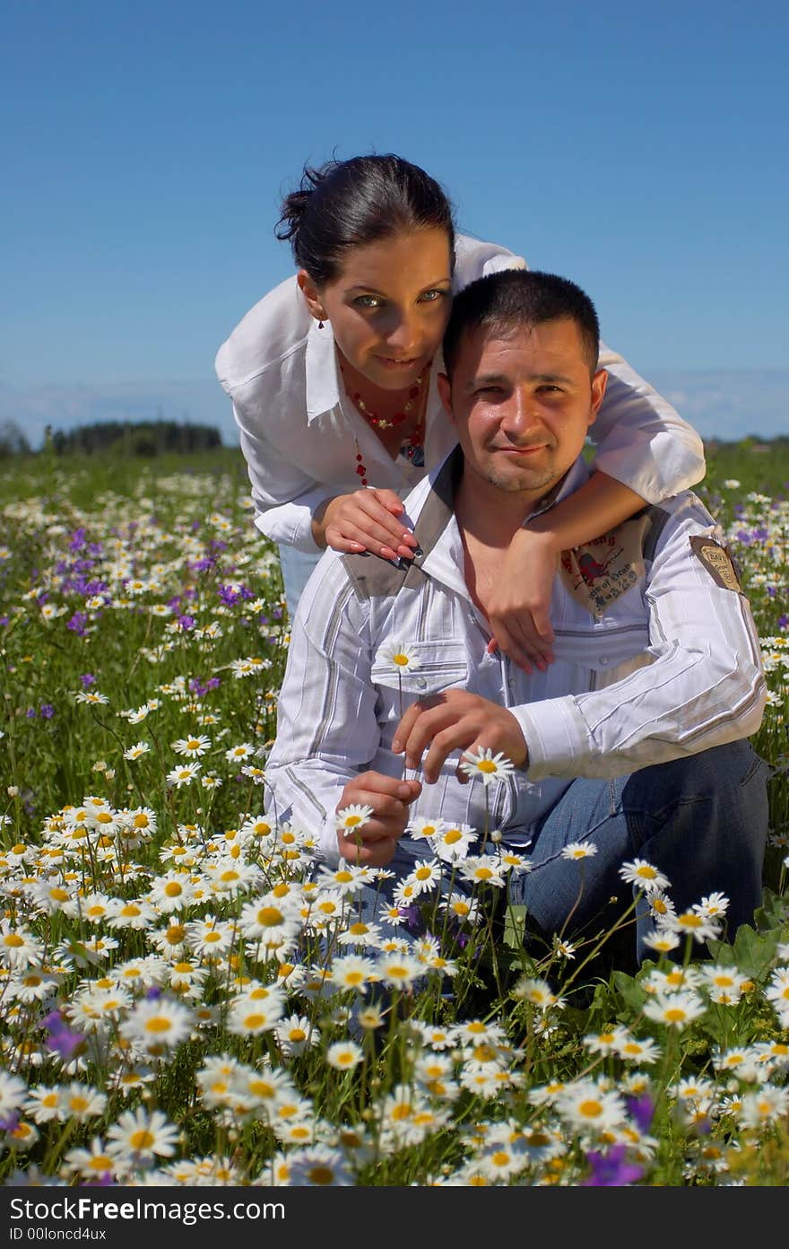 Young happy couple at the sunny day in a field with camomiles and handbells