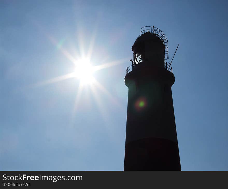 Looking up at Portland Bill Lighthouse, Dorset, England, silhouetted against blue sky.