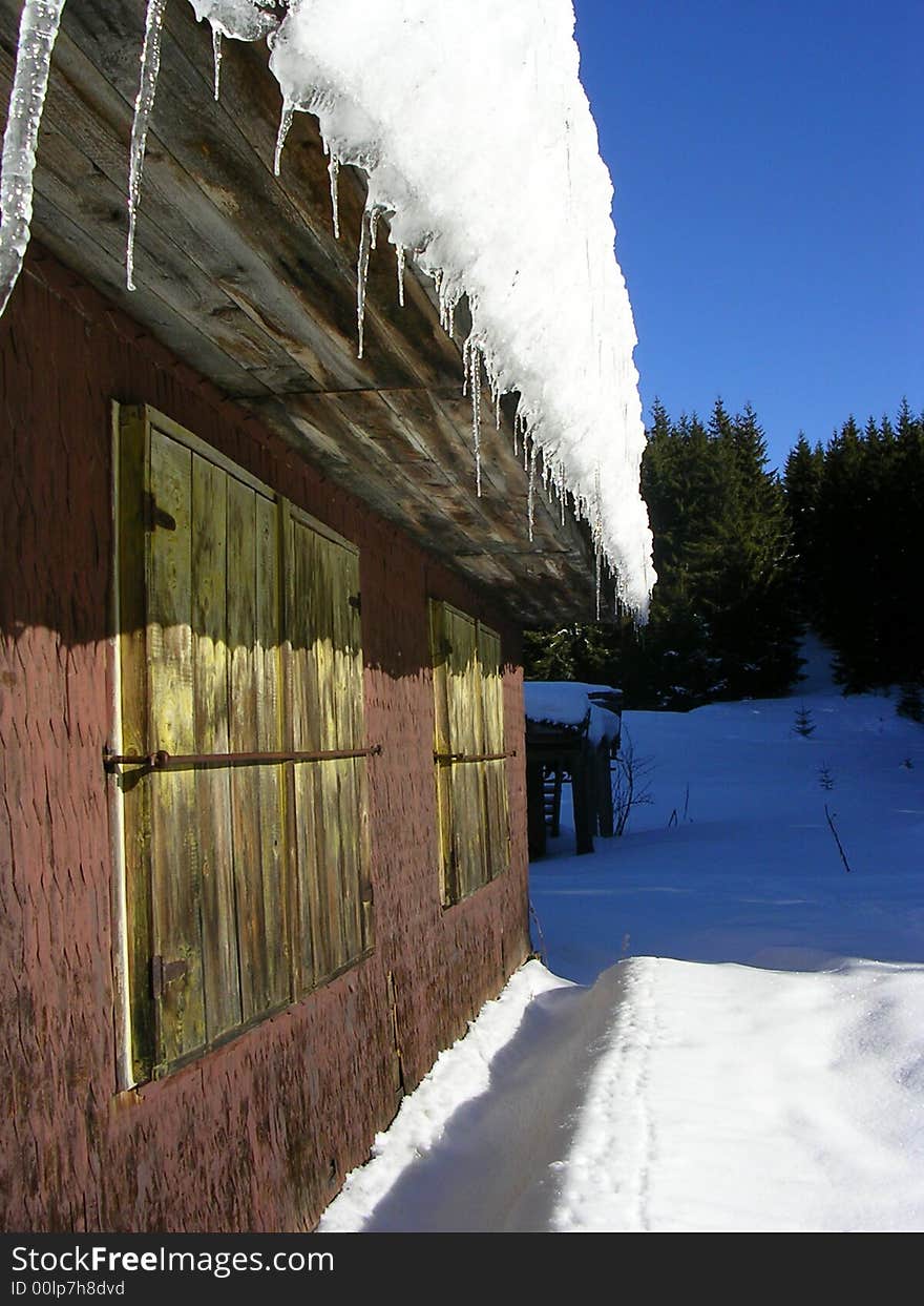 Wooden cottage in mountains weigh in to snow with icicles