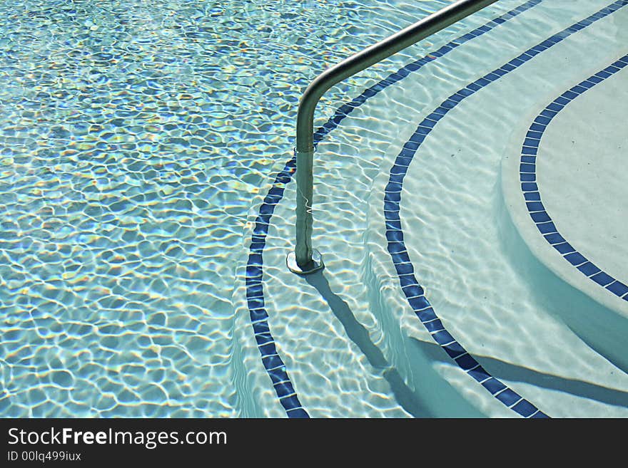 Swimming pool steps and rail with the rippling warm blue waters