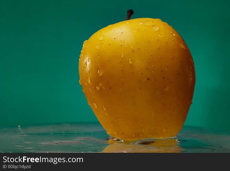 Yellow apple on the glass over green background