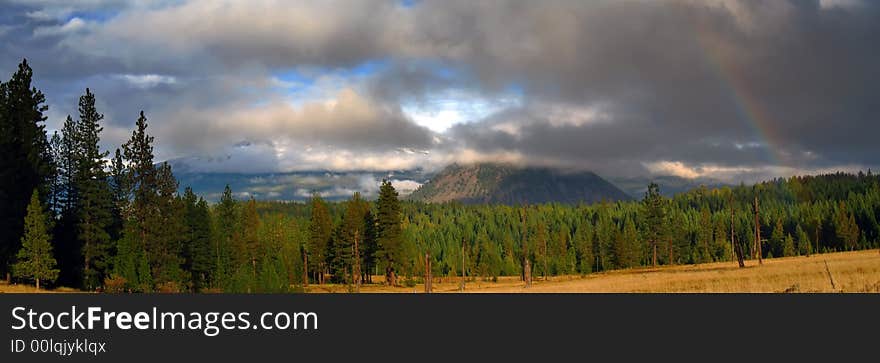 Clouds and rainbow over mountains, meadow, evergreen trees and autumn grass. Clouds and rainbow over mountains, meadow, evergreen trees and autumn grass