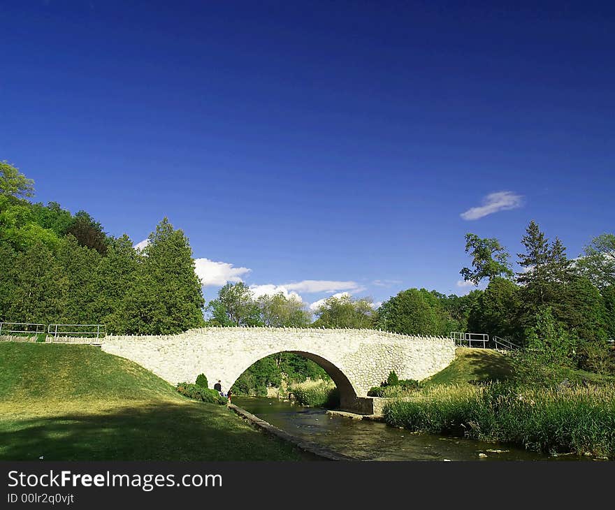 A pretty arched stone bridge over a shallow stream under a blue sky.