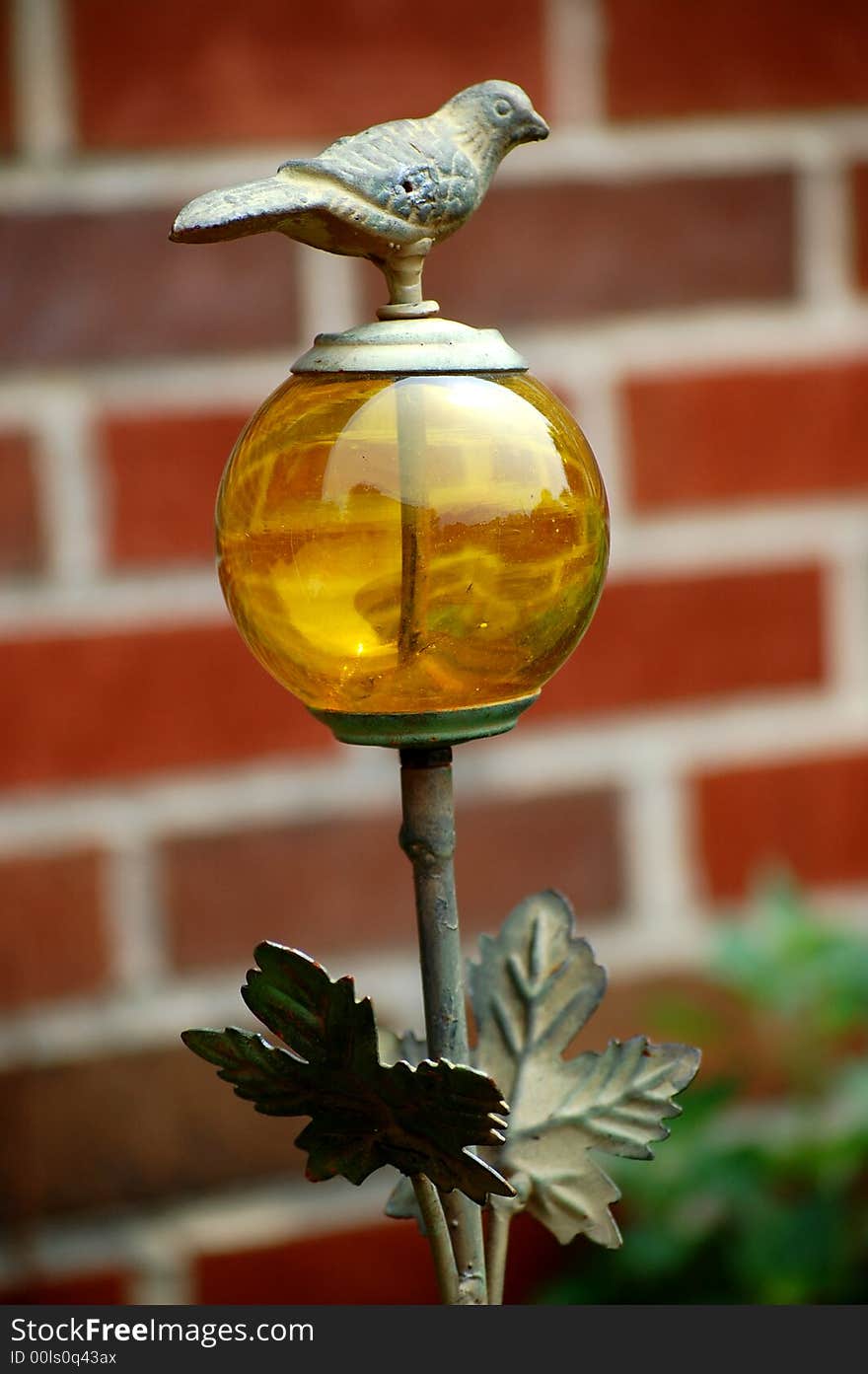 Wrought iron bird on yellow globe lawn ornament against a brick background. Wrought iron bird on yellow globe lawn ornament against a brick background