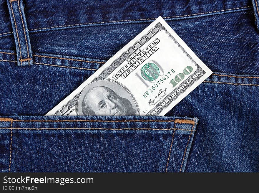 A one hundred dollar bill in the back pocket of denim trousers.  Photographed in a studio. A one hundred dollar bill in the back pocket of denim trousers.  Photographed in a studio.