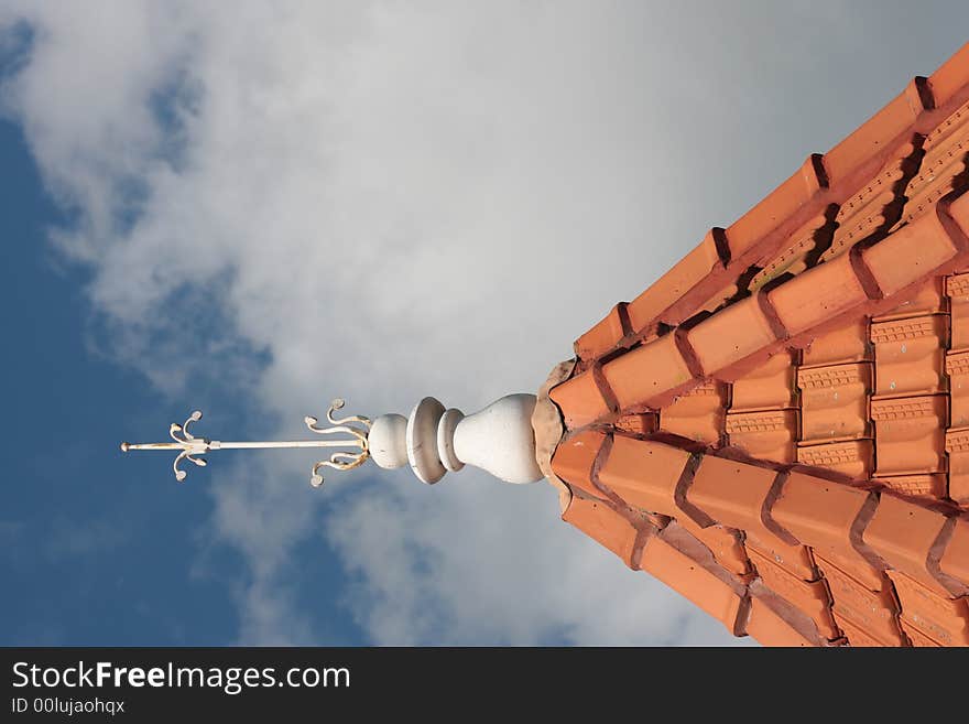 Decorative lightening rod on the top of a tiled tower roof.  Blue sky background. Decorative lightening rod on the top of a tiled tower roof.  Blue sky background