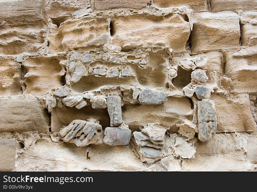 Weathered ancient stone wall, the soft stone and masonry eroded by the passage of time and the effects of rain and wind