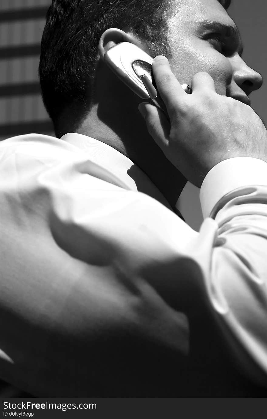 Black and white one young businessman holding cellphone to ear with building structure in background. Black and white one young businessman holding cellphone to ear with building structure in background