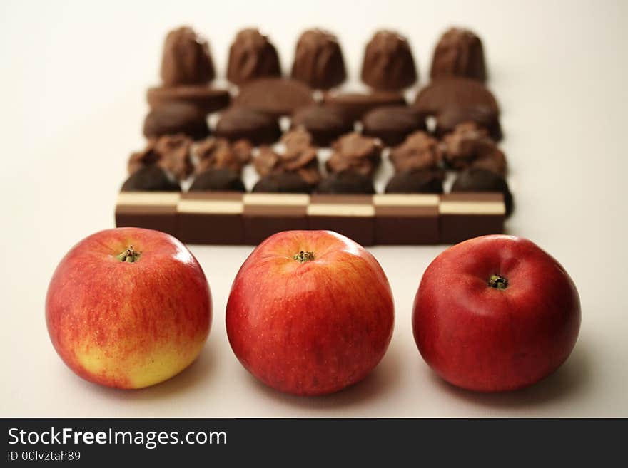 Three apples standing opposite chocolate pralines in the background. Three apples standing opposite chocolate pralines in the background.