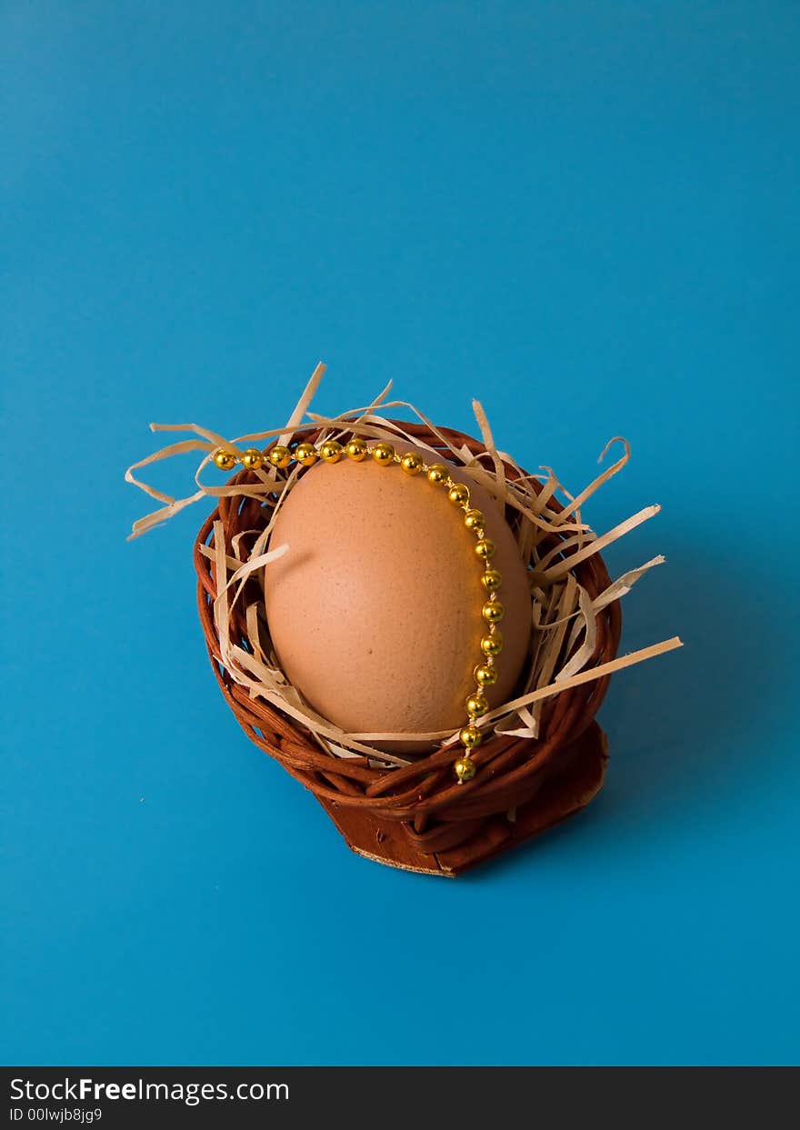 Egg in basket with beads and shavings on blue background. Egg in basket with beads and shavings on blue background