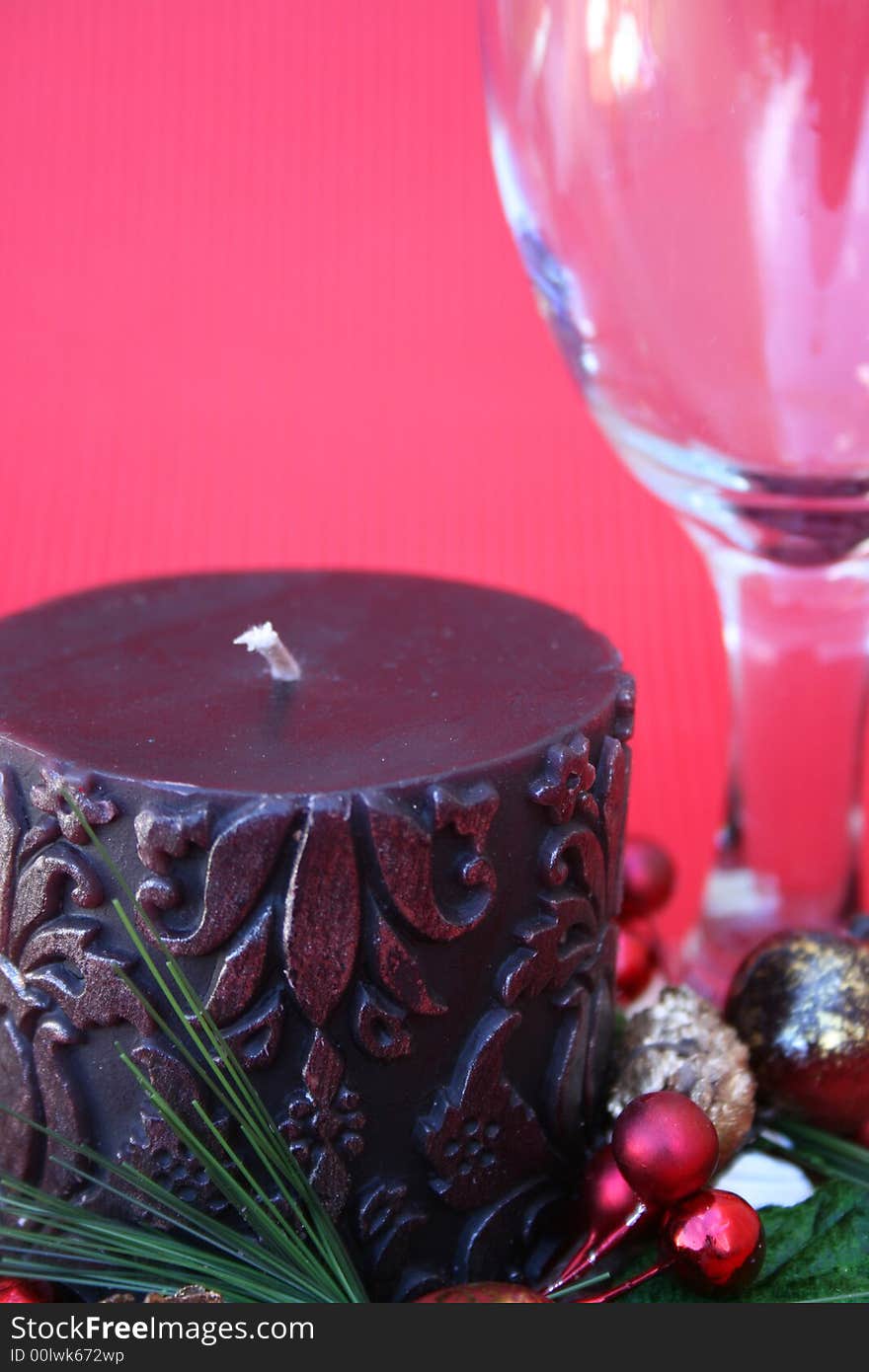 Dark candle with a christmas wreath and a wine glass on a red background. Dark candle with a christmas wreath and a wine glass on a red background