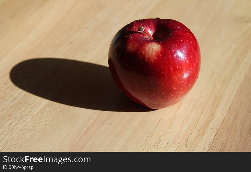 A single apple with hard lighting and a shadow